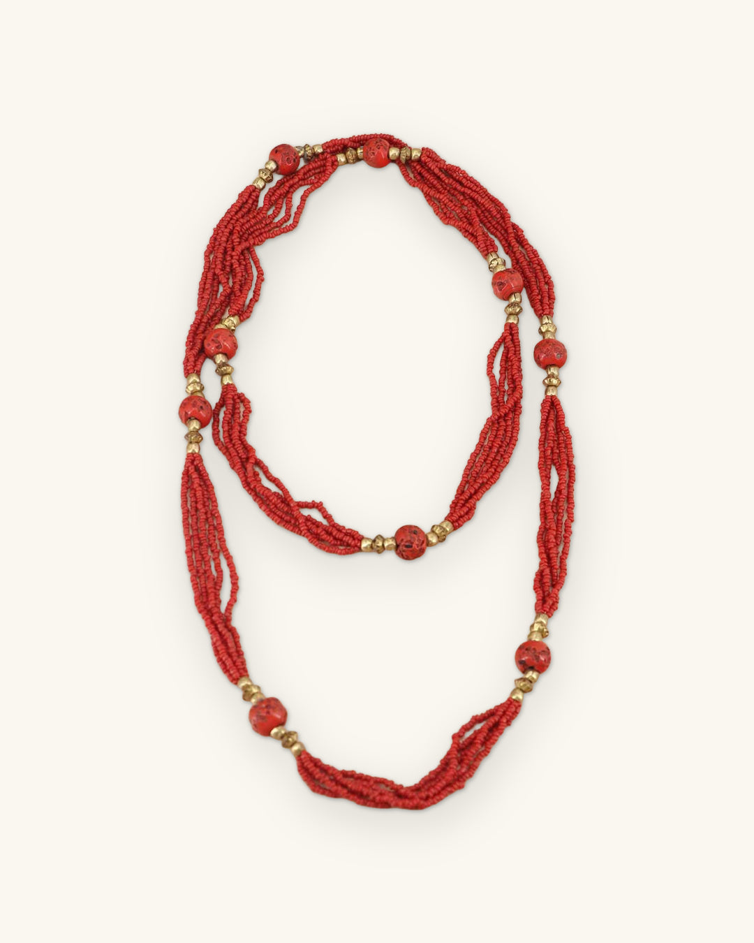 Red seed bead rope necklace doubled into two loops, showing a layered wear option with red and brass-tone accent beads, shown on a sand background