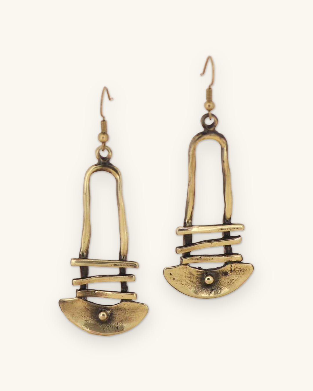 Bronze dangle earrings with arch, bars and half-moon shapes, hand-forged metalwork from Türkiye, on blush pink, shown on a sand background