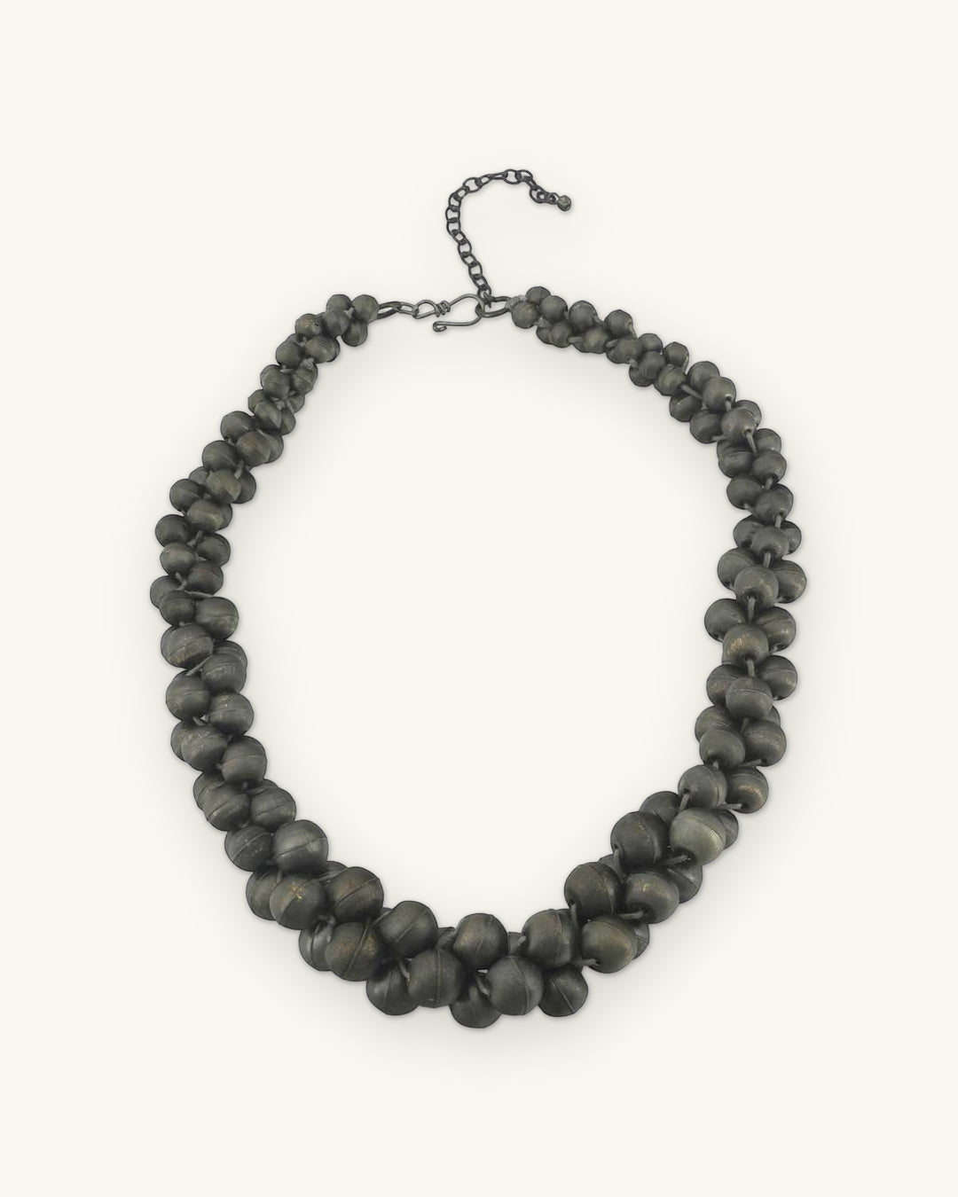 Full view of the dark gunmetal-tone twisted bead rope necklace with clasp and chain extender, shown on a sand background