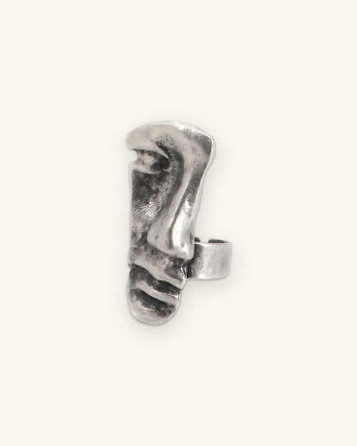 Close-up of the antique silver-tone face ring with textured brow, nose and ridged lips, shown on a sand background