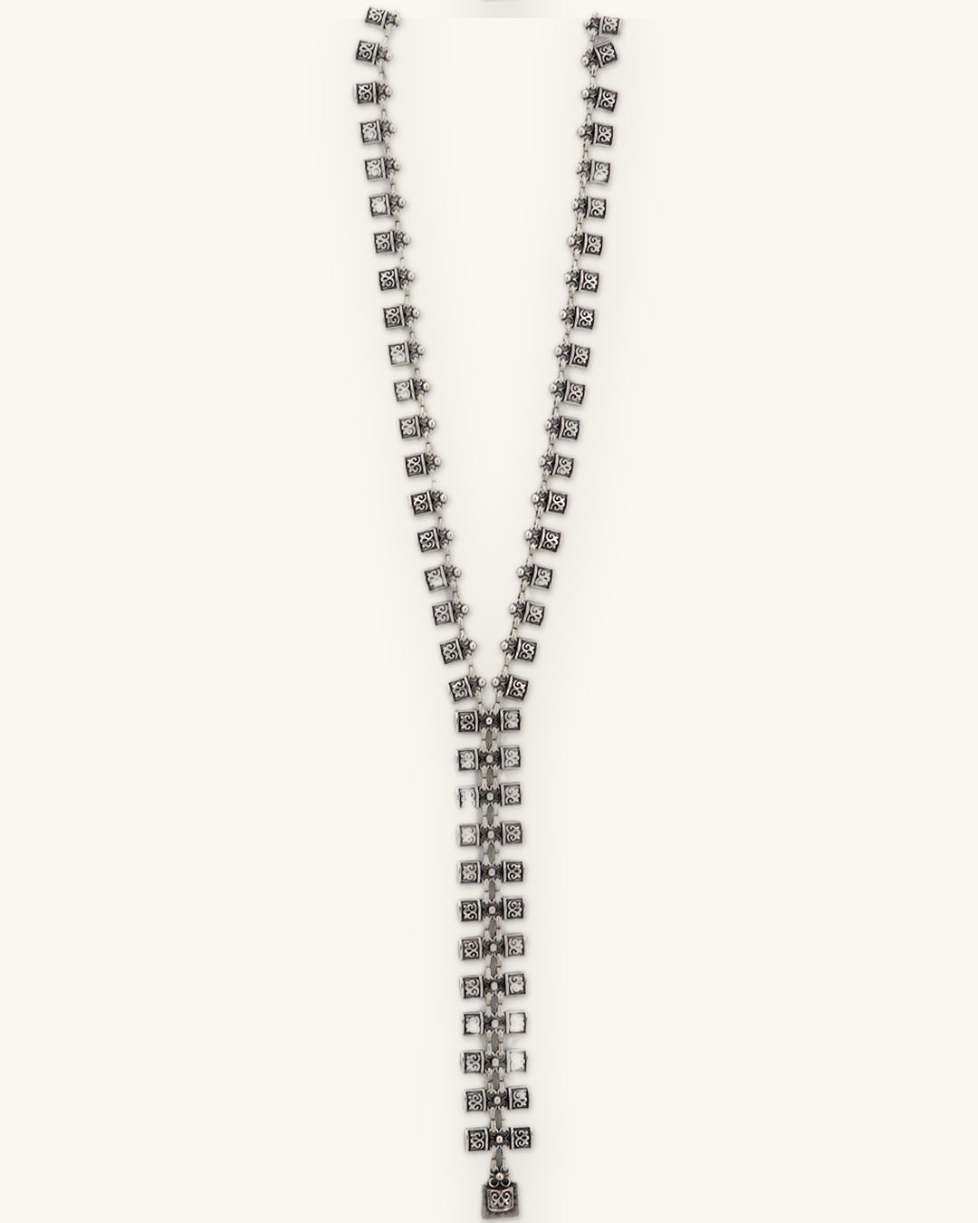 Scroll-stamped square link Y-necklace laid straight to show the long center drop, shown on a sand background