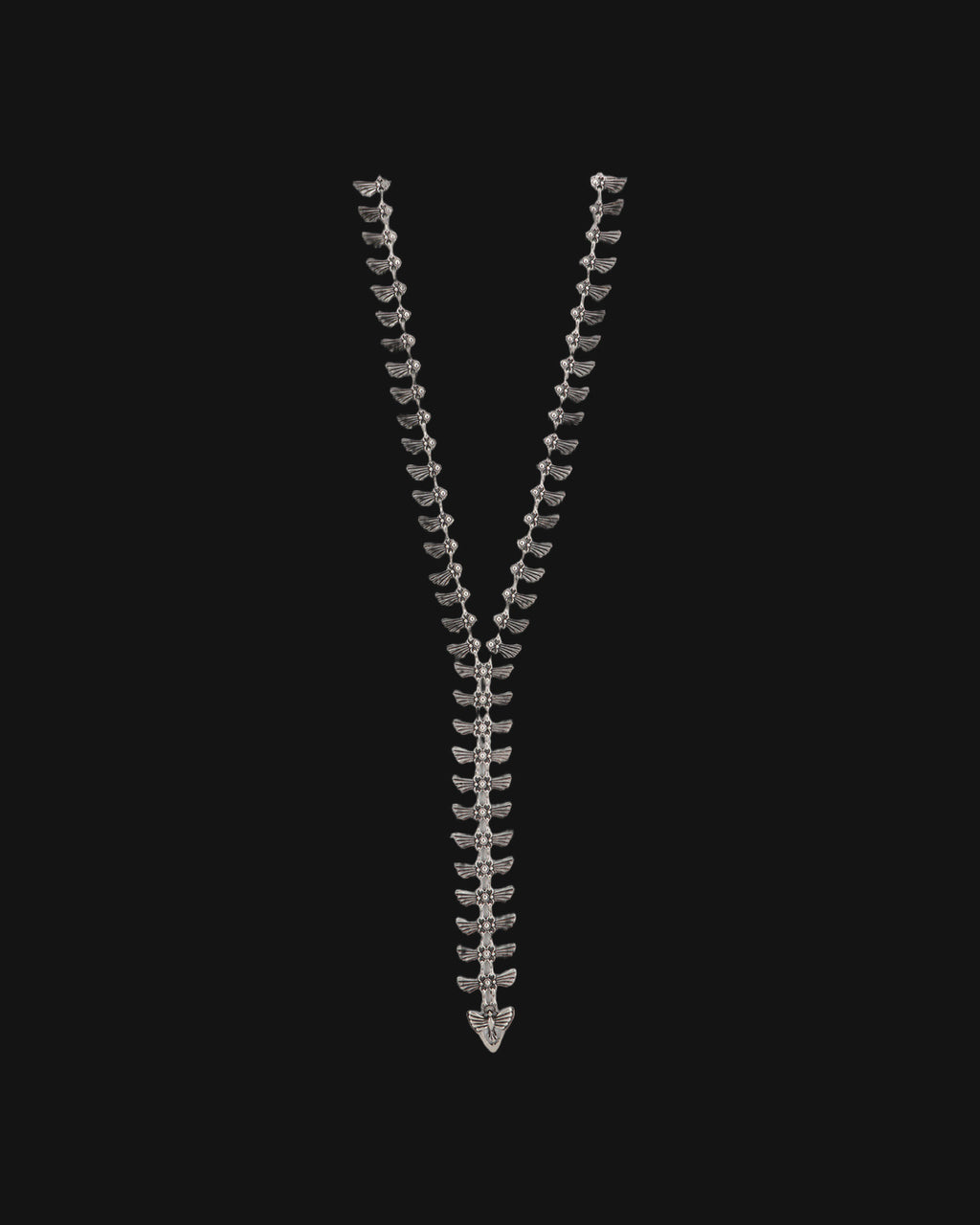 Winged-tab silver Y-necklace laid straight with a winged charm at the end of the drop, shown on a black background