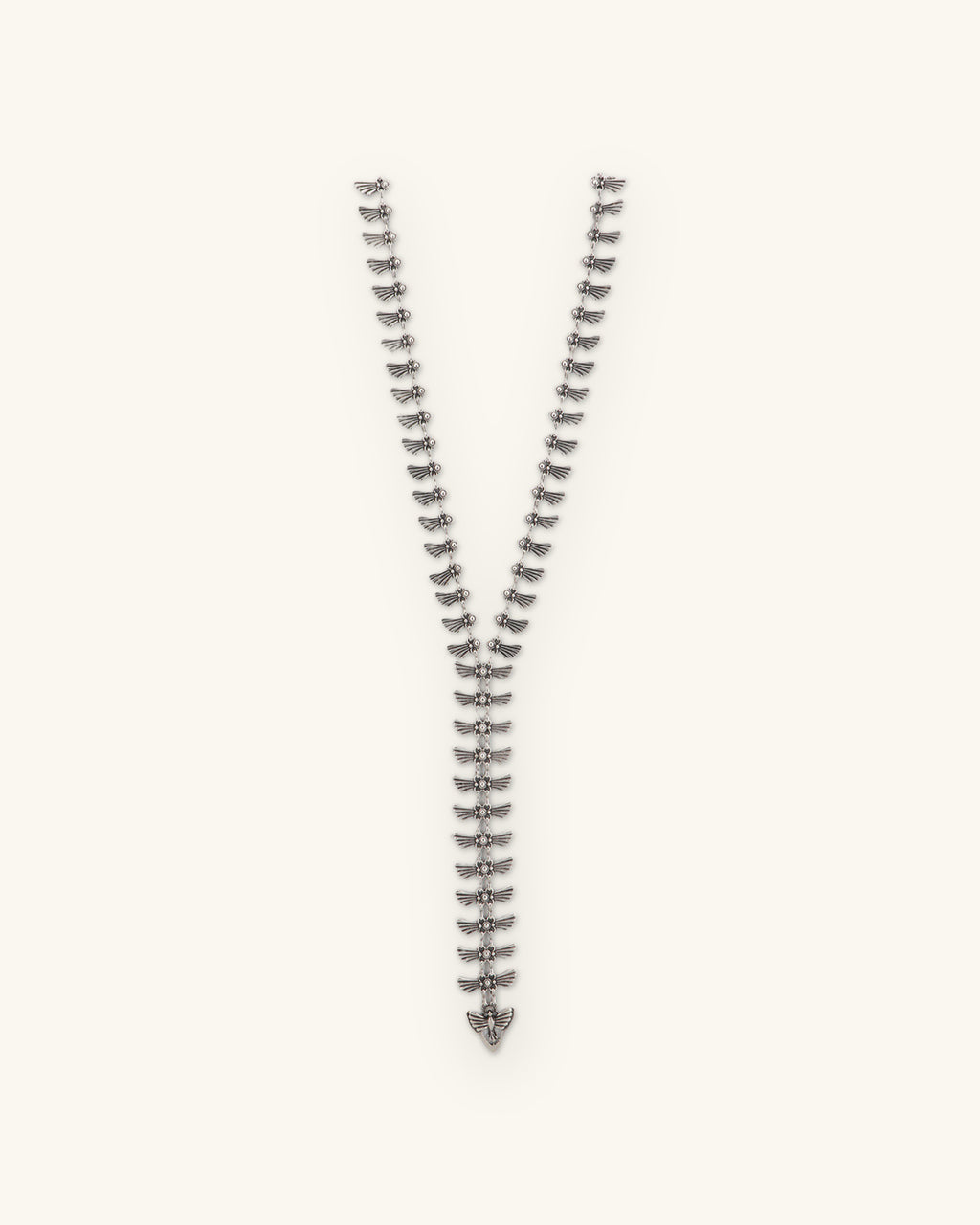 Winged-tab silver Y-necklace laid straight with a winged charm at the end of the drop, shown on a sand background