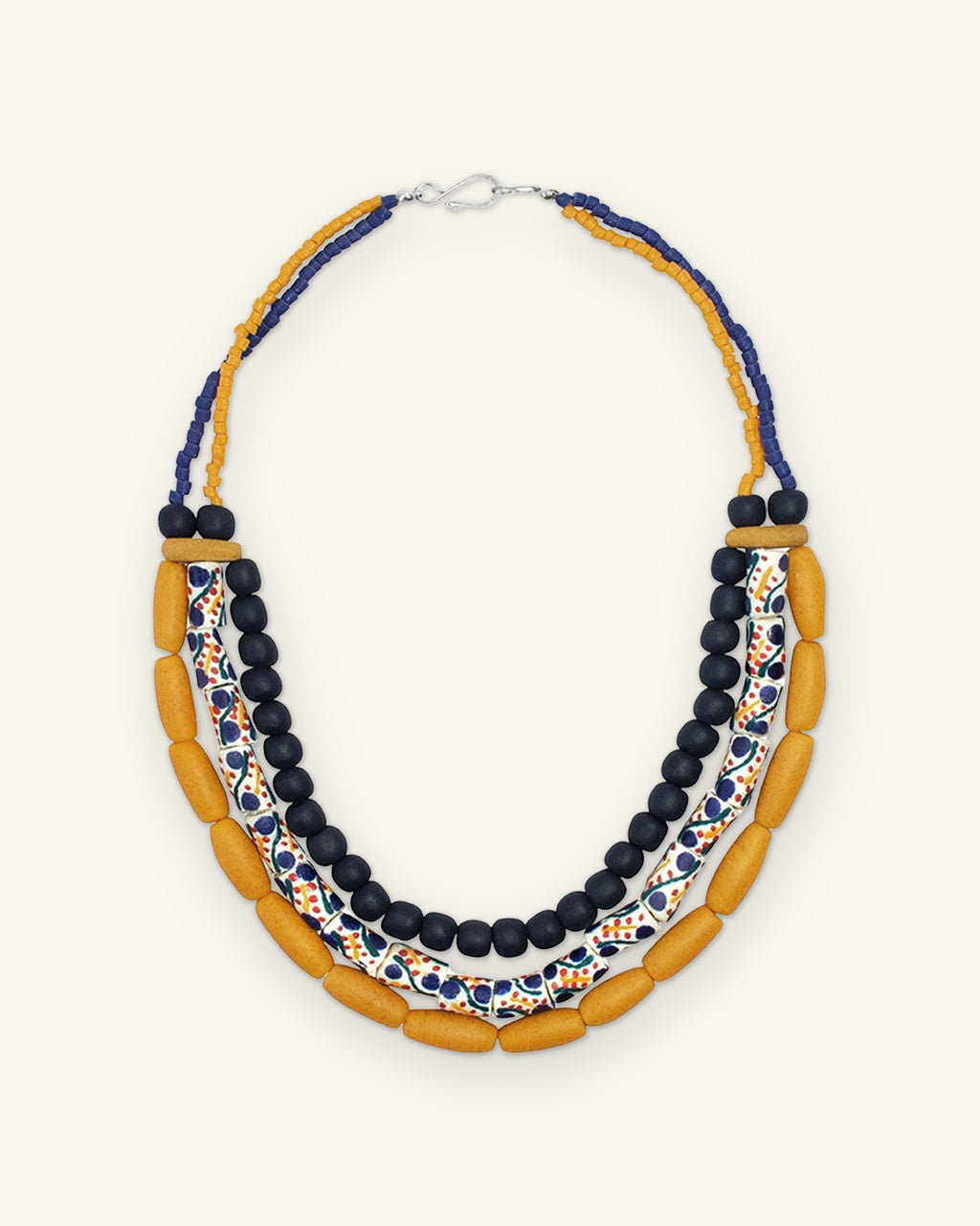 Full view of the asymmetric three-row glass bead necklace with navy and mustard seed bead strands at the back, shown on a sand background