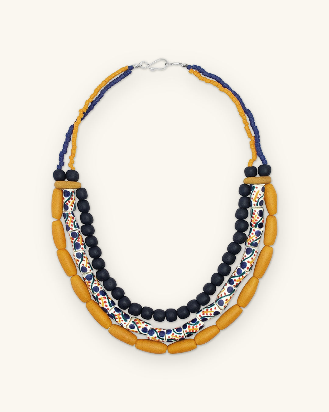 Full view of the asymmetric three-row glass bead necklace with navy and mustard seed bead strands at the back, shown on a sand background