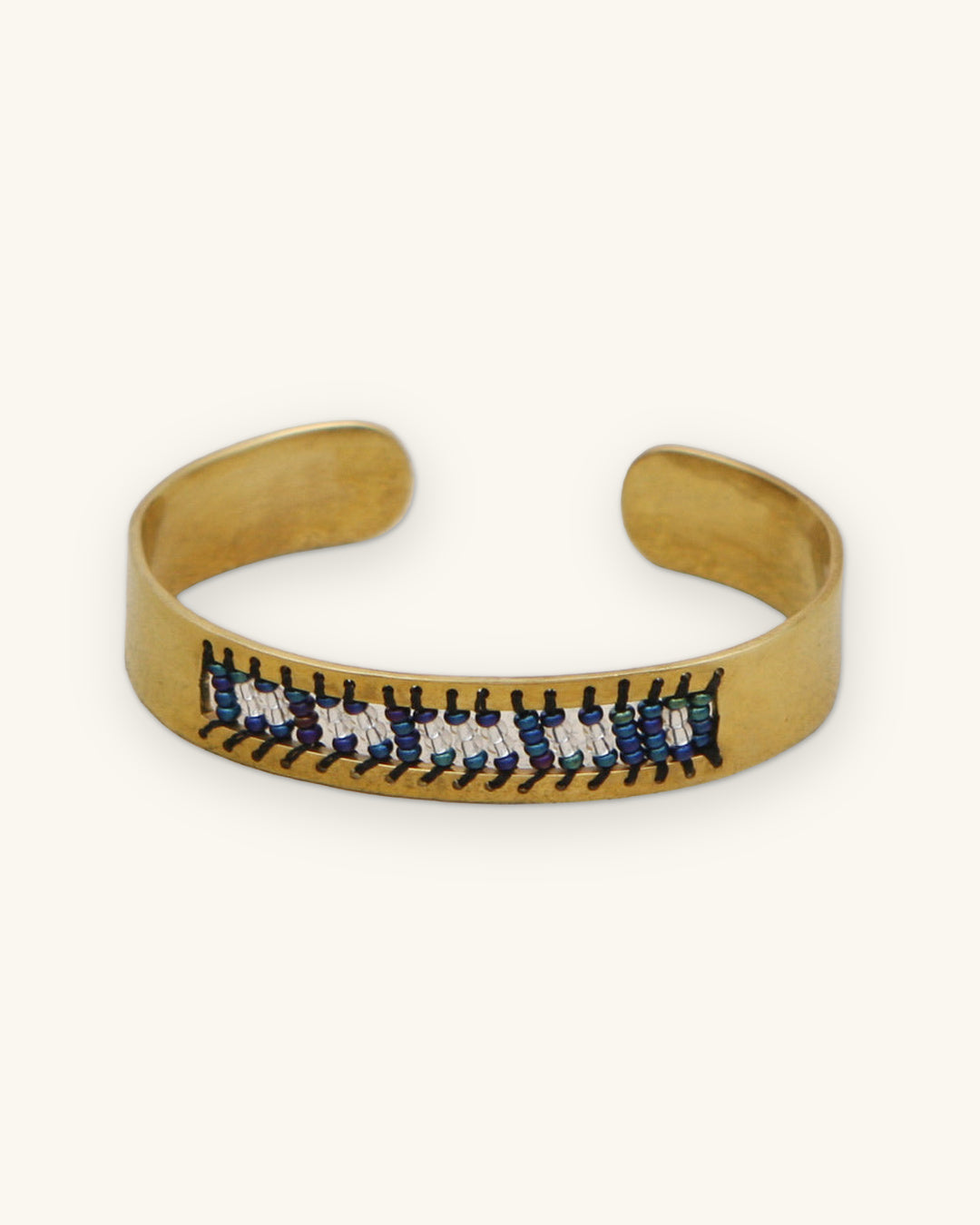 Brass cuff bracelet with blue, white and black glass seed bead Morse code band, beaded in Kenya, shown on a sand background