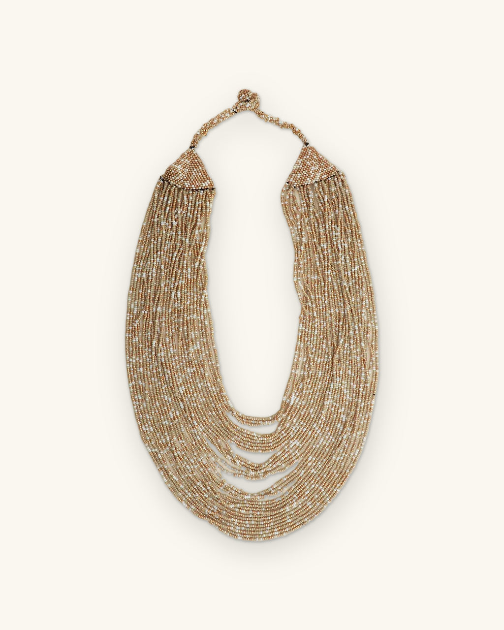 Beige and gold glass seed bead cascade necklace laid flat, strands hanging from a woven beaded top band, shown on a sand background