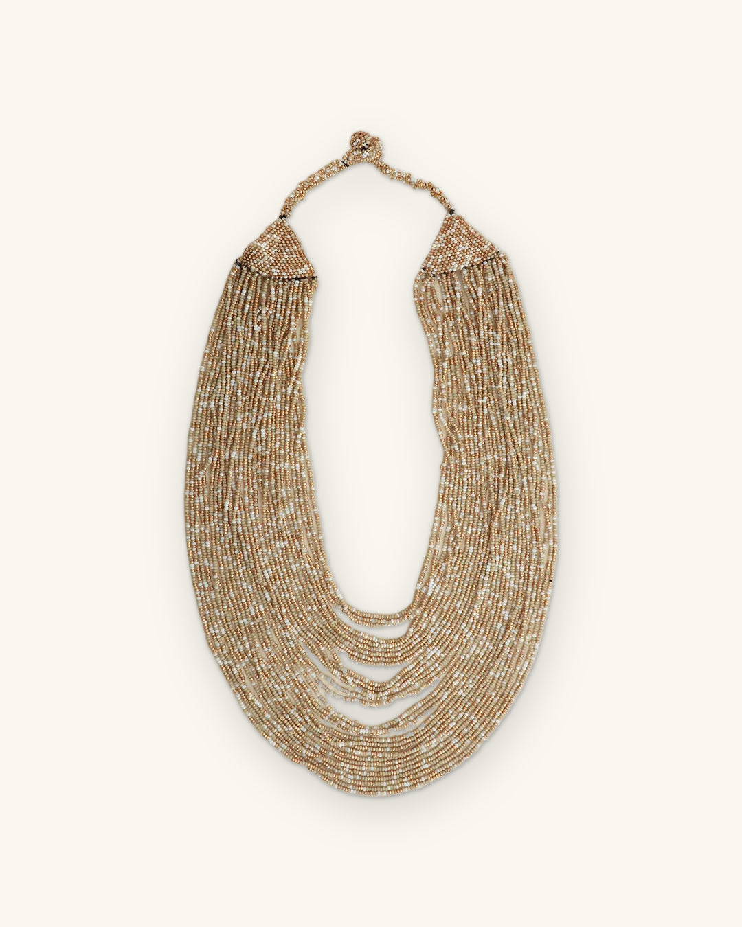 Beige and gold glass seed bead cascade necklace laid flat, strands hanging from a woven beaded top band, shown on a sand background