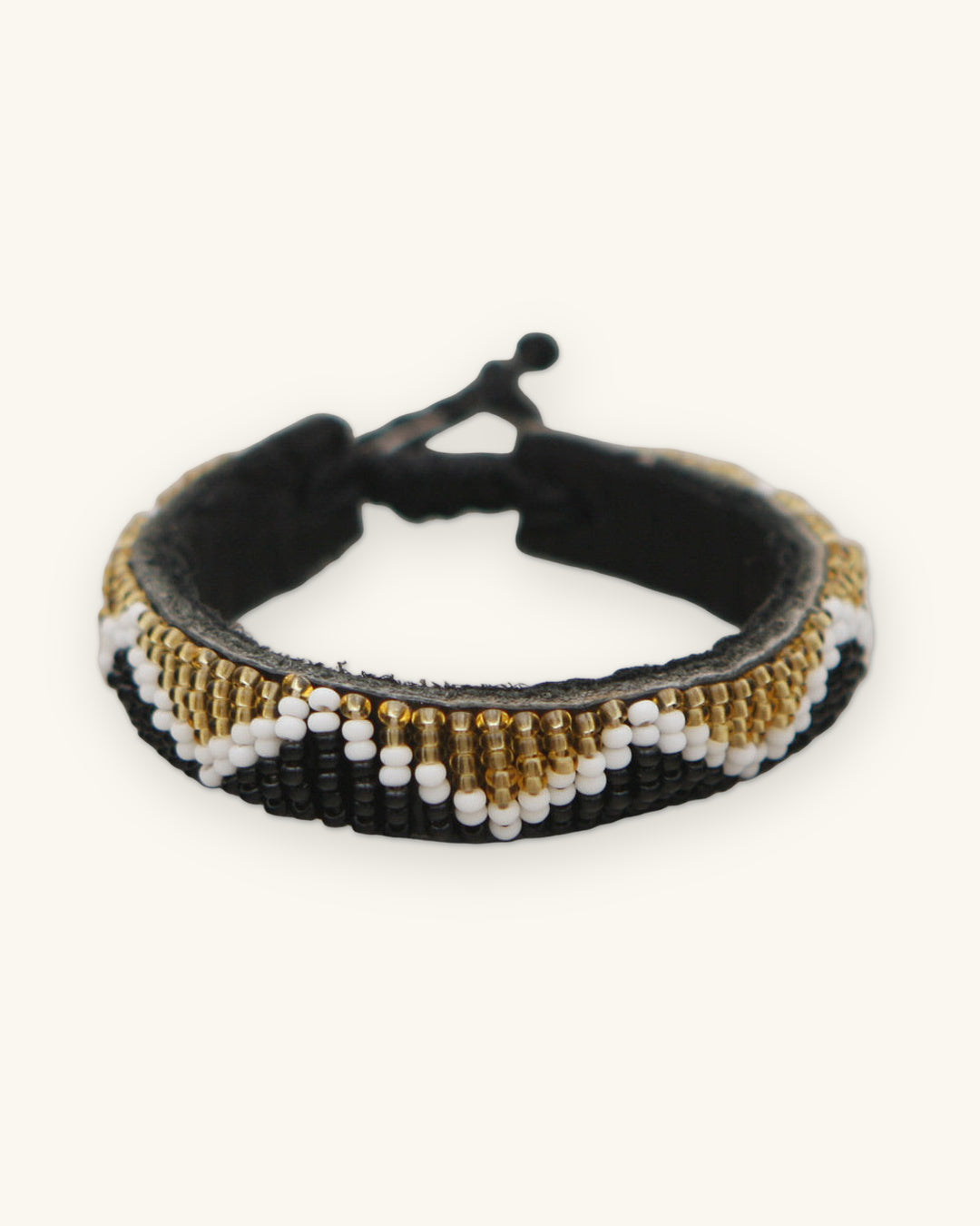 Zigzag beaded leather cuff in black, gold and white Czech glass seed beads, Kenyan beadwork, shown on a sand background