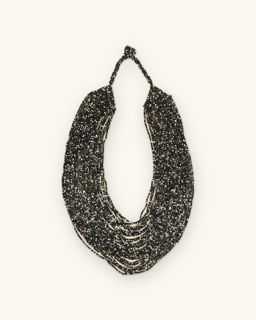 Cascading multi-strand black glass seed bead necklace with silver flecks, hand-strung in India, laid flat, shown on a sand background