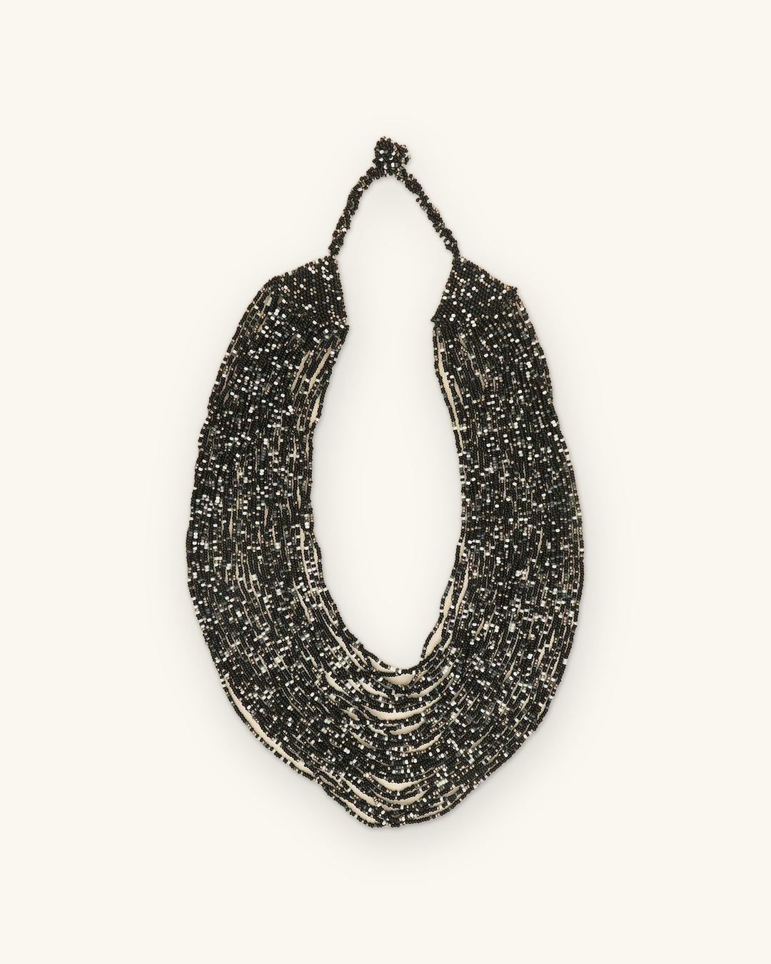 Cascading multi-strand black glass seed bead necklace with silver flecks, hand-strung in India, laid flat, shown on a sand background