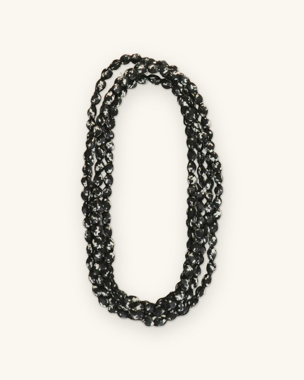 Black and white printed fabric bead necklace coiled into a triple loop, shown on a sand background