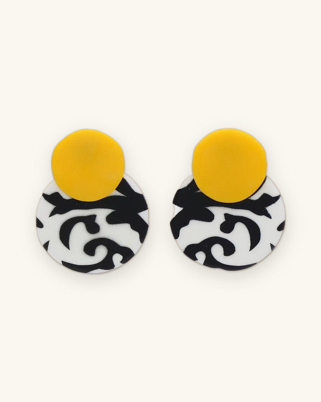 Double-disc drop earrings with a yellow top disc over a black and white swirl disc, hand-painted resin from the Philippines, shown on a sand background