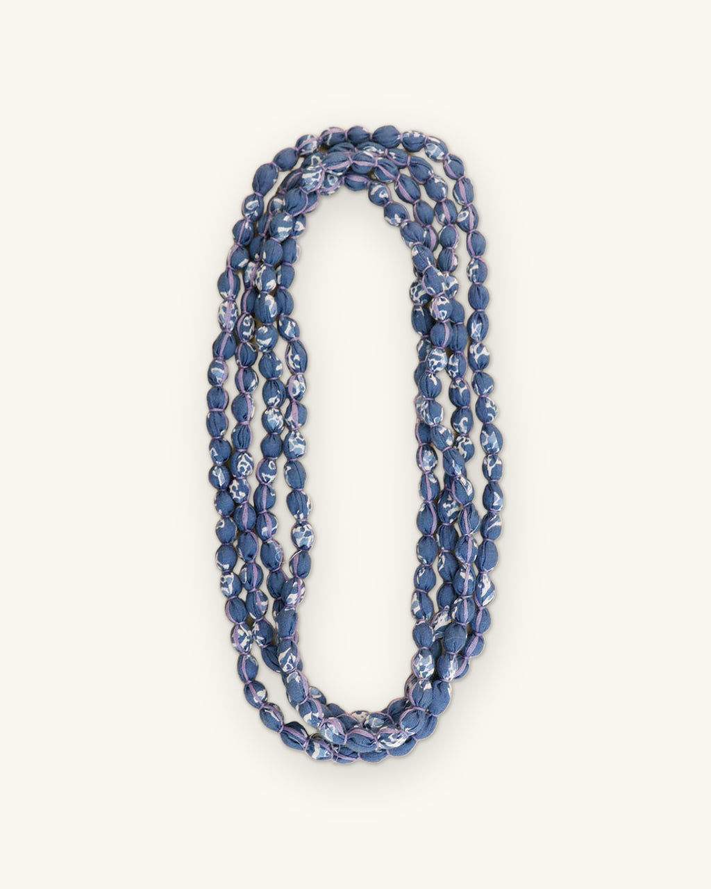 Blue printed fabric bead necklace folded into a narrow triple loop, shown on a sand background