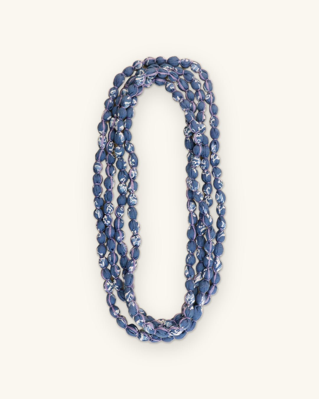 Blue printed fabric bead necklace folded into a narrow triple loop, shown on a sand background