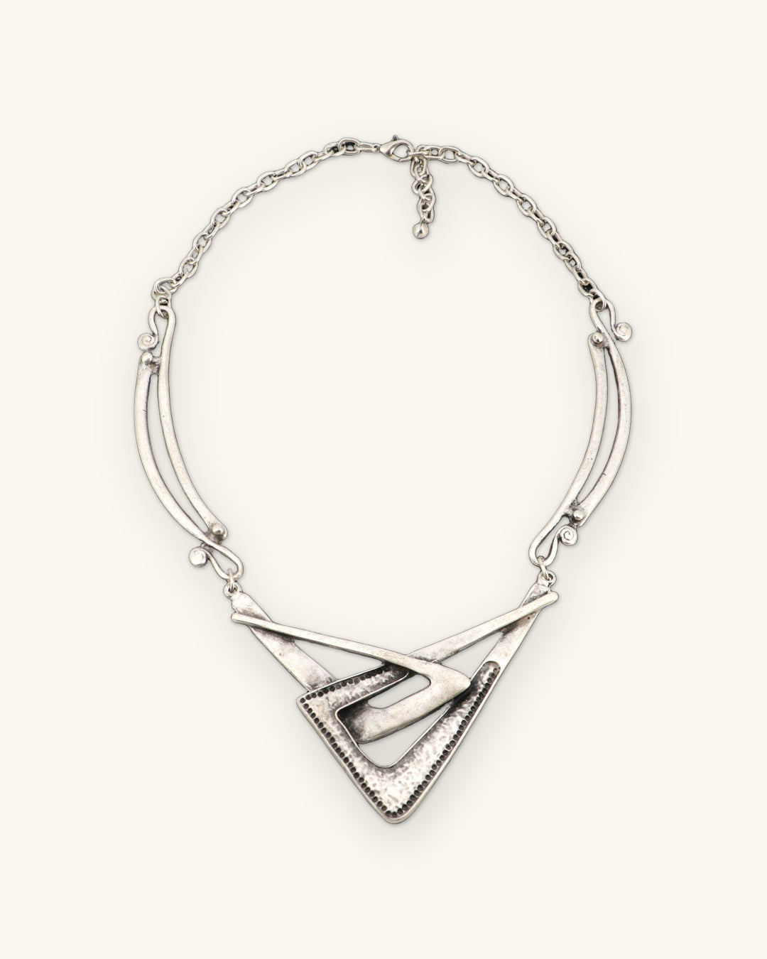 Full view of the interlocking chevron necklace with curved side bars, cable chain and extender on slate gray, shown on a sand background
