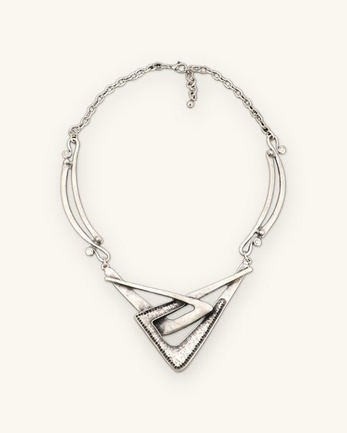Full view of the interlocking chevron necklace with curved side bars, cable chain and extender on slate gray, shown on a sand background