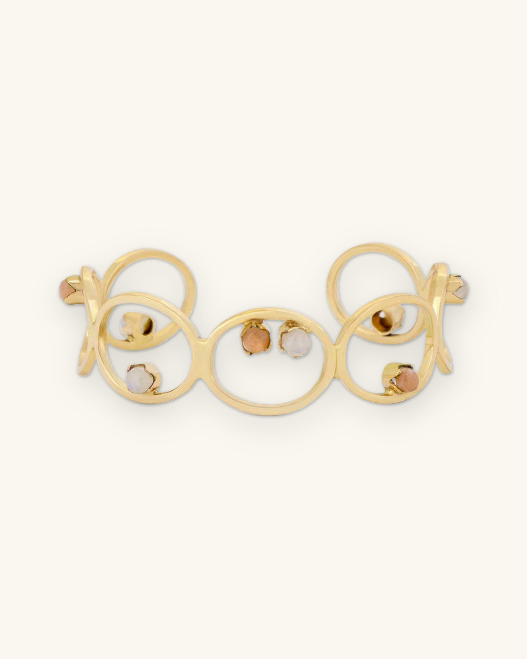 Linked-circle brass cuff bracelet set with white and peach moonstones, made in India, front view, shown on a sand background