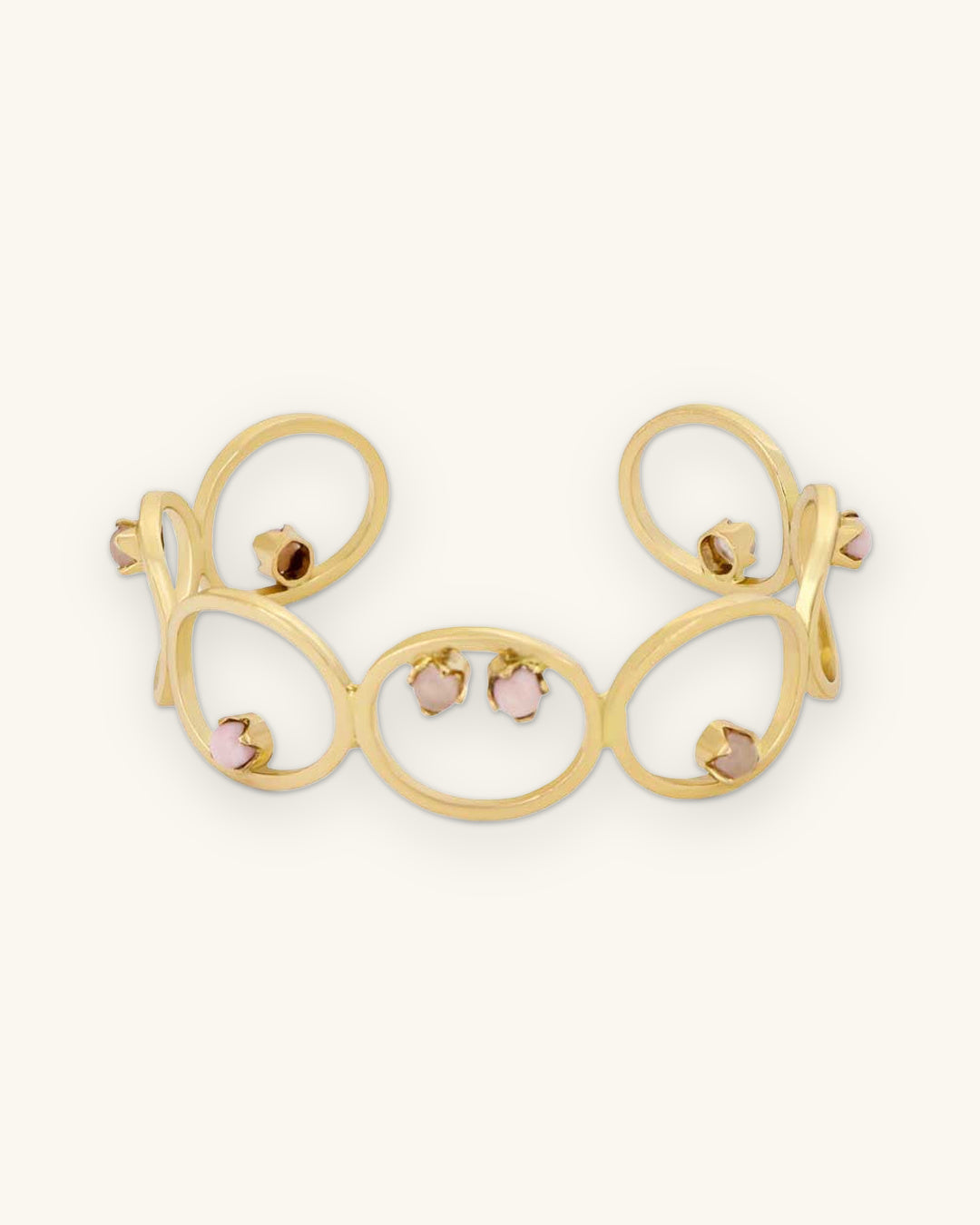 Open-loop brass cuff bracelet with opal and rose quartz cabochons, made in India, front view, shown on a sand background