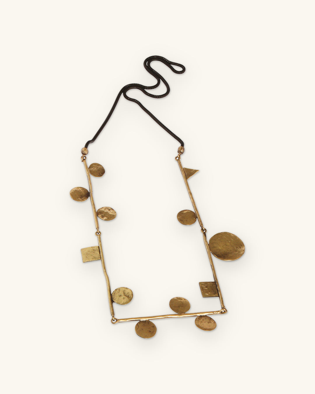 Rectangular bronze bar frame pendant hung with hammered round discs, squares and a triangle, on black cord, shown on a sand background