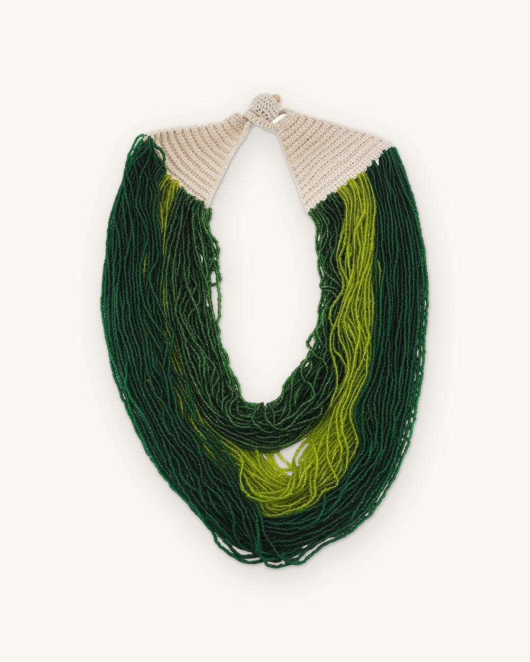 Green multi-strand bead necklace laid flat with cream crocheted cotton ends and button closure, shown on a sand background
