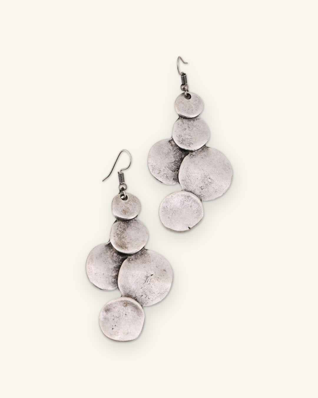 Pair of silver-tone hammered disc earrings with graduated overlapping discs on fish-hook wires, shown on a sand background