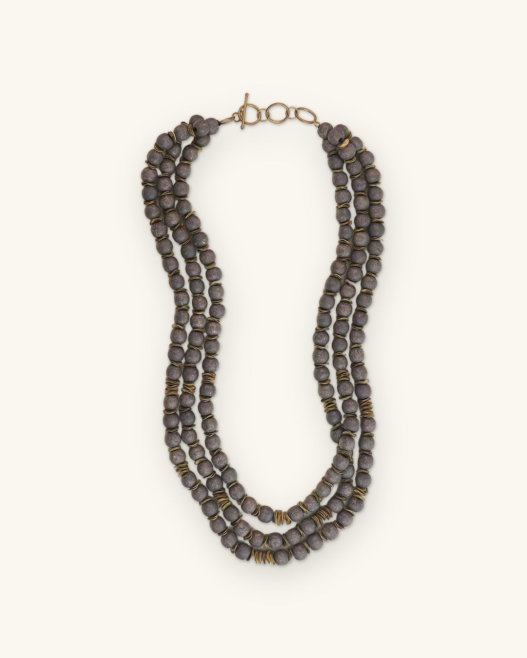 Three-strand charcoal gray wood bead necklace with brass spacers and toggle clasp, made in India, shown on a sand background