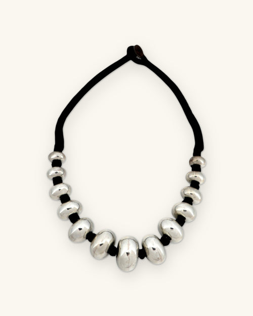 Full view of the silver rondelle necklace with black cord and loop closure, shown on a sand background
