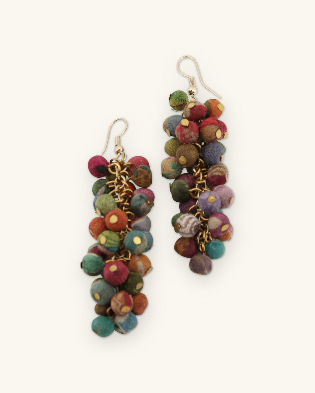 Angled view of the multicolor Kantha bead cluster earrings showing brass chain links between the beads, shown on a sand background