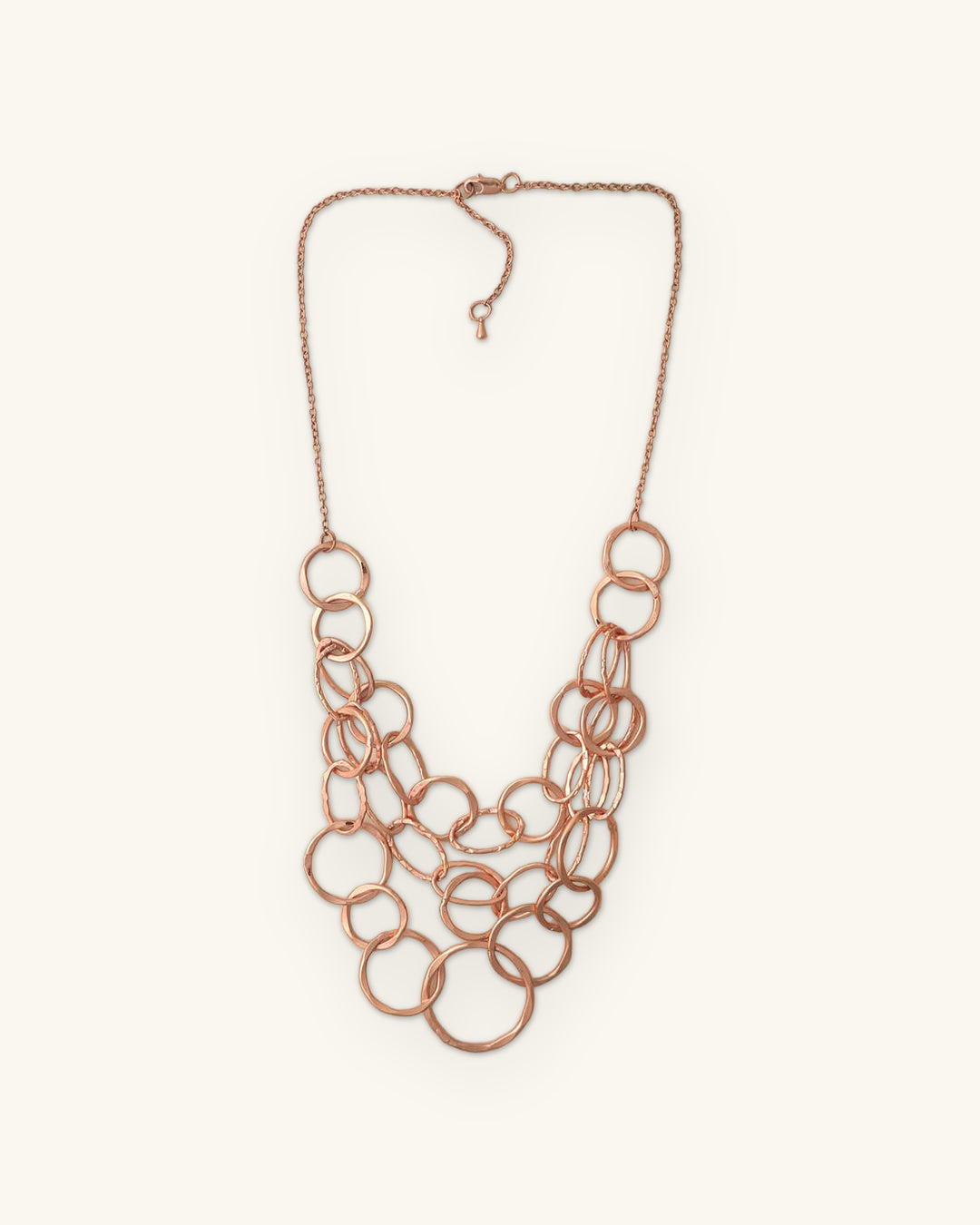 Layered bib of linked hammered copper rings on a fine copper chain with lobster clasp, shown on a sand background