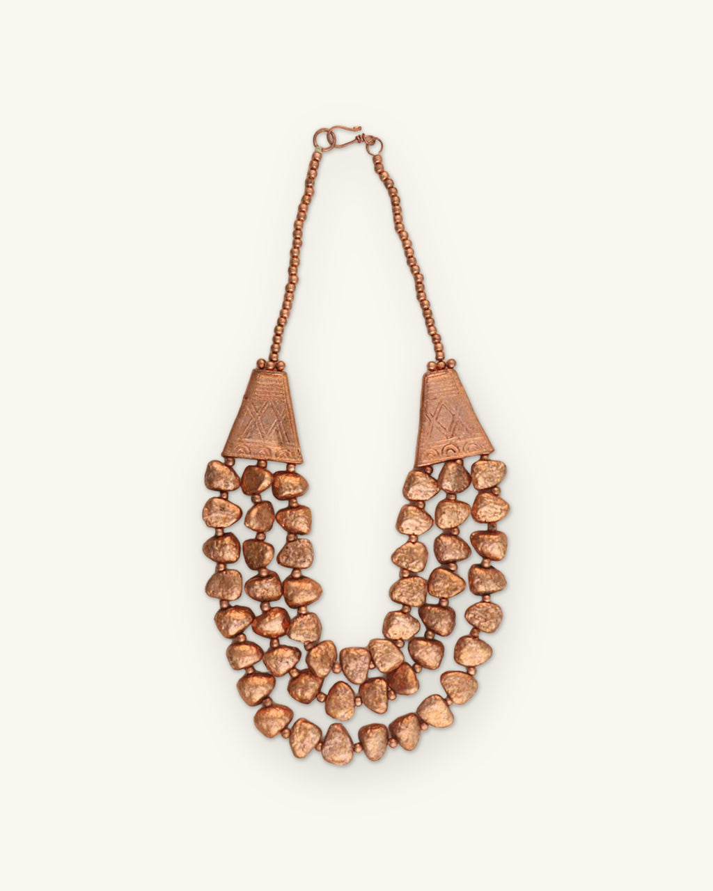 Triple-strand copper-tone nugget necklace with engraved cone ends, hand-textured and antiqued in India, shown on a sand background