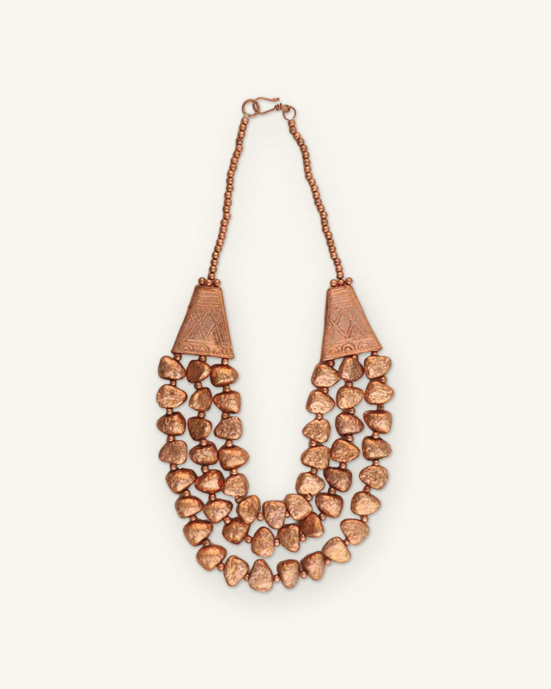 Triple-strand copper-tone nugget necklace with engraved cone ends, hand-textured and antiqued in India, shown on a sand background