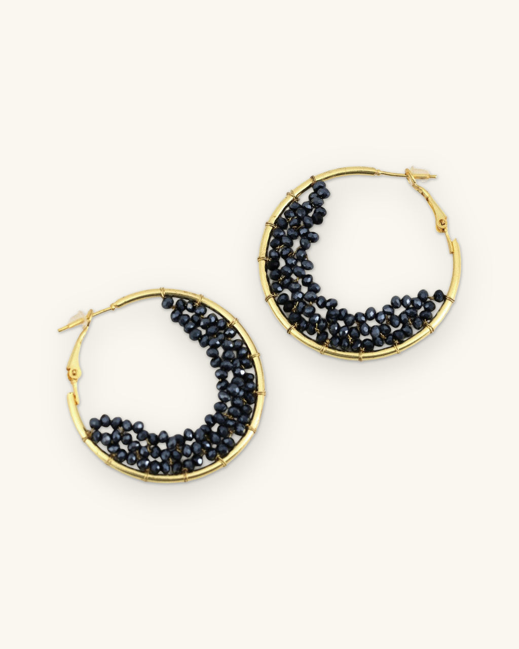 Gold-plated brass hoop earrings filled with a crescent of faceted black glass beads, hand-wrapped in India, shown on a sand background