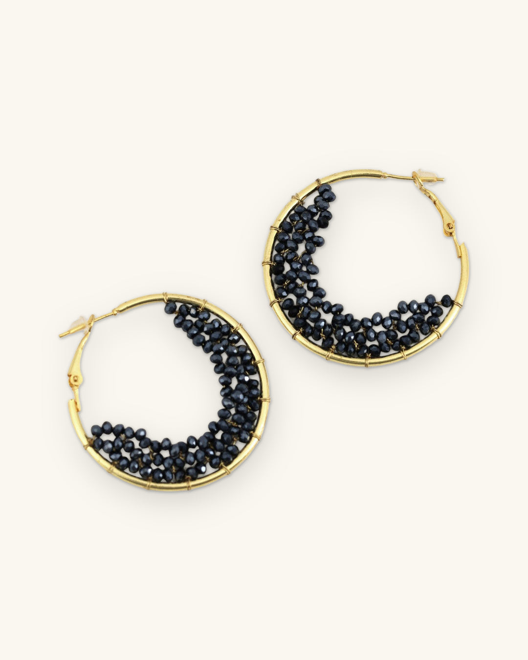 Gold-plated brass hoop earrings filled with a crescent of faceted black glass beads, hand-wrapped in India, shown on a sand background