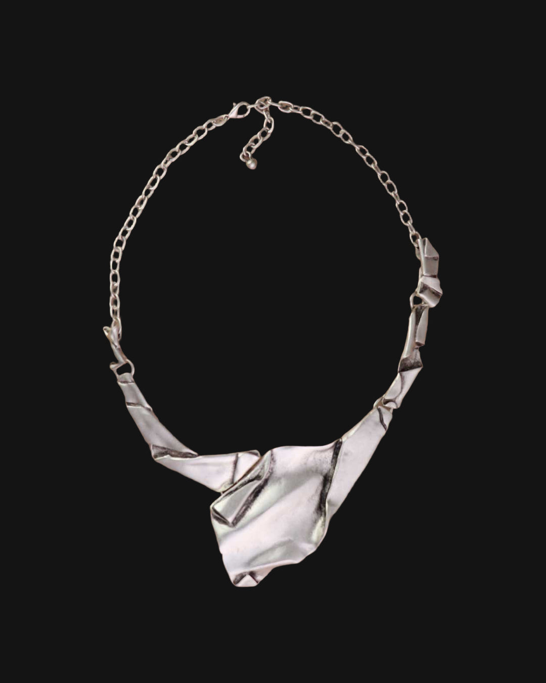 Full view of the crumpled-paper style silver-tone bib necklace with folded links and cable chain, shown on a black background
