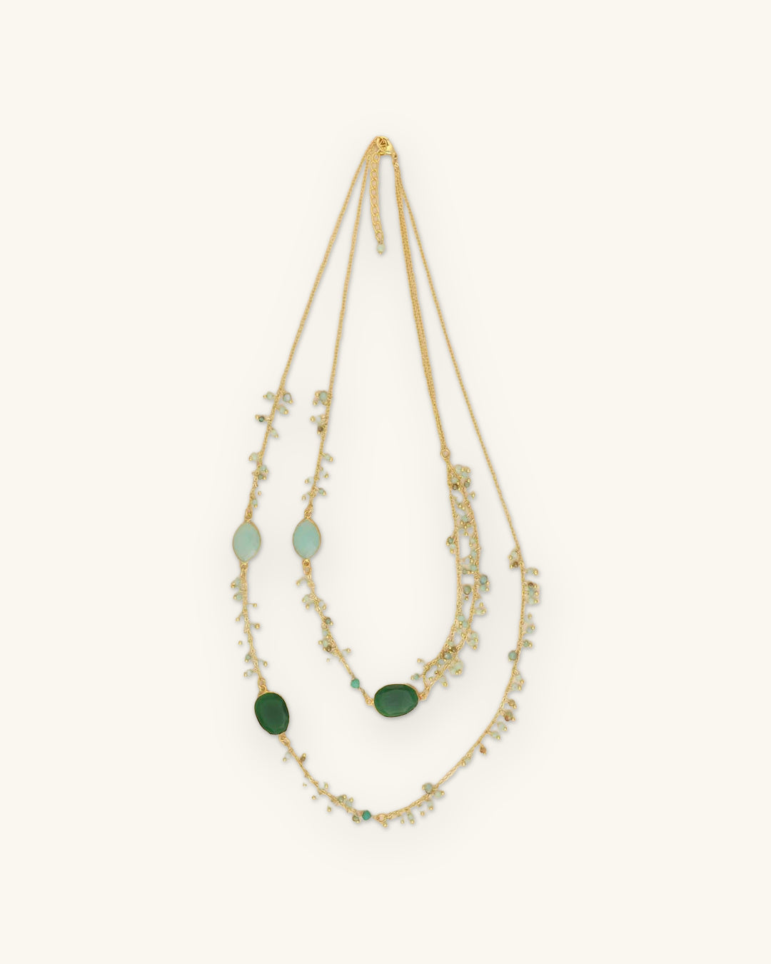 Two-layer gold-plated necklace in Blue/Green with aqua and deep green inset stones and bead drops, shown on a sand background