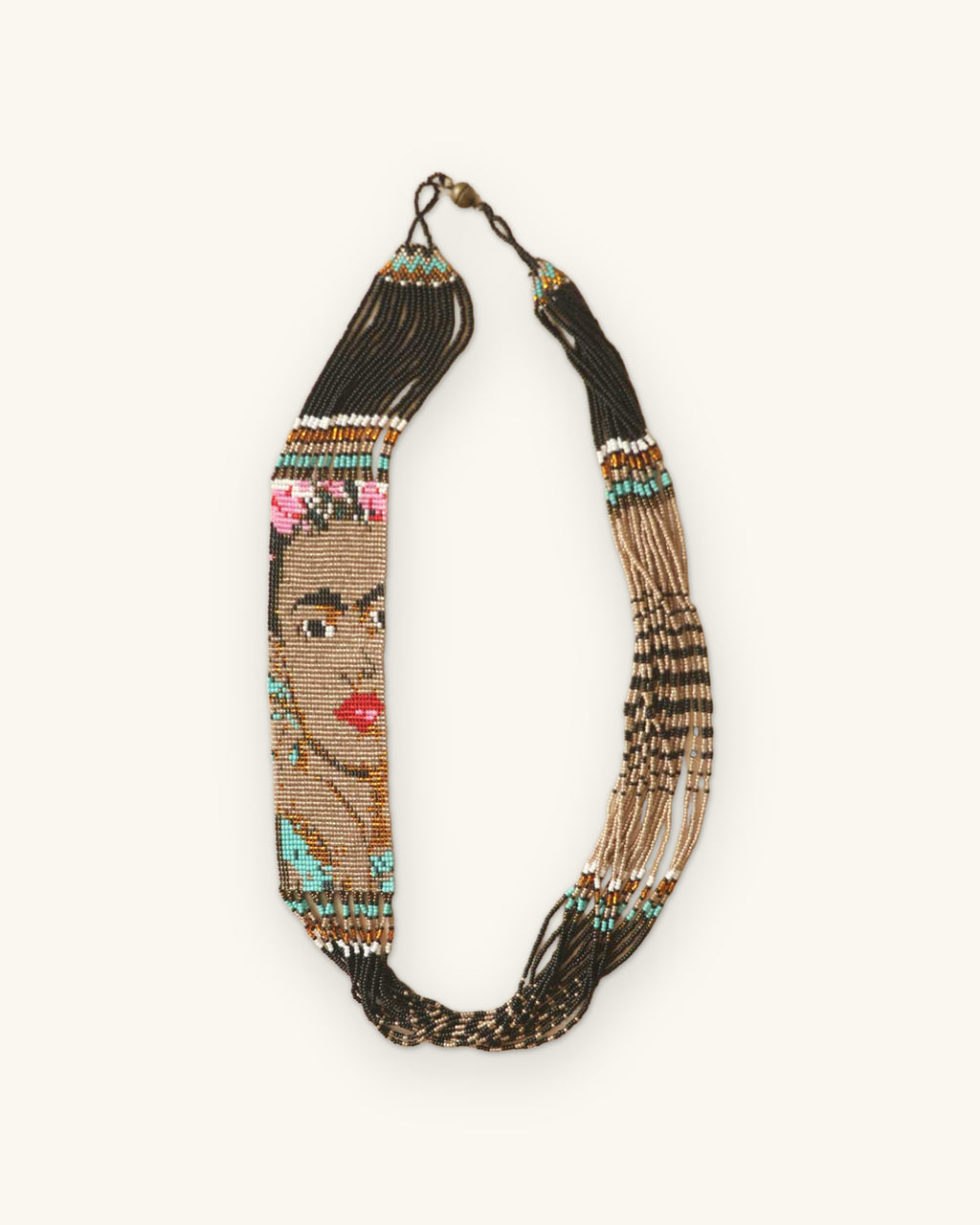 Loom-woven bead necklace with Frida Kahlo portrait panel, flower crown and red lips, laid flat with black strand fringe, shown on a sand background