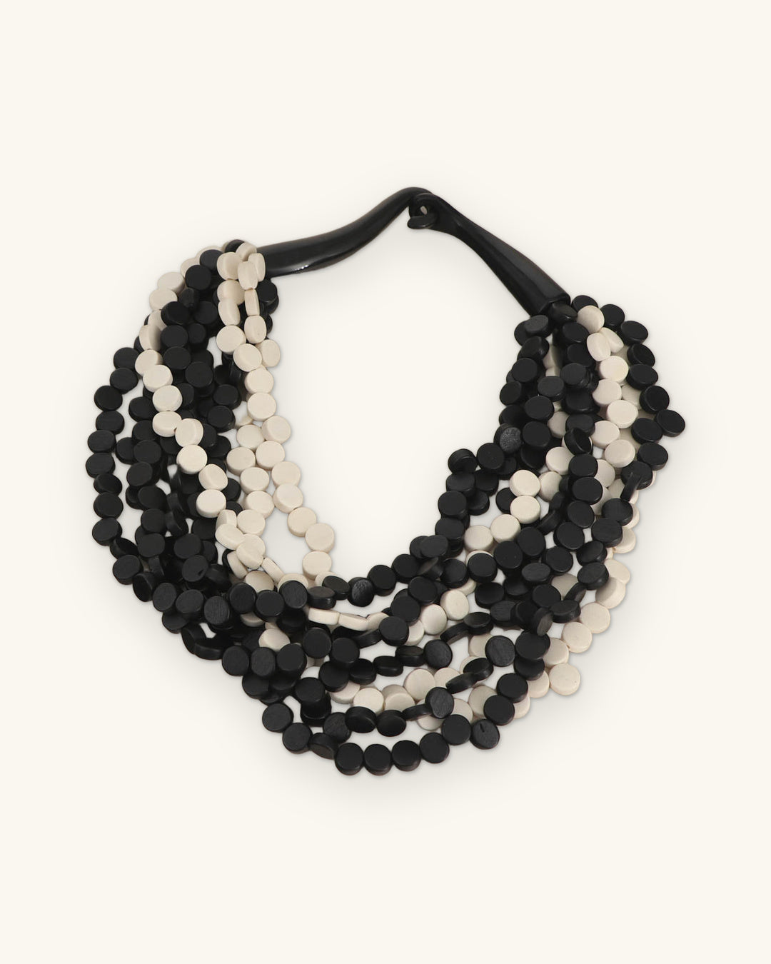 Nine-strand black and white wood disc necklace with a black horn clasp, laid flat, shown on a sand background