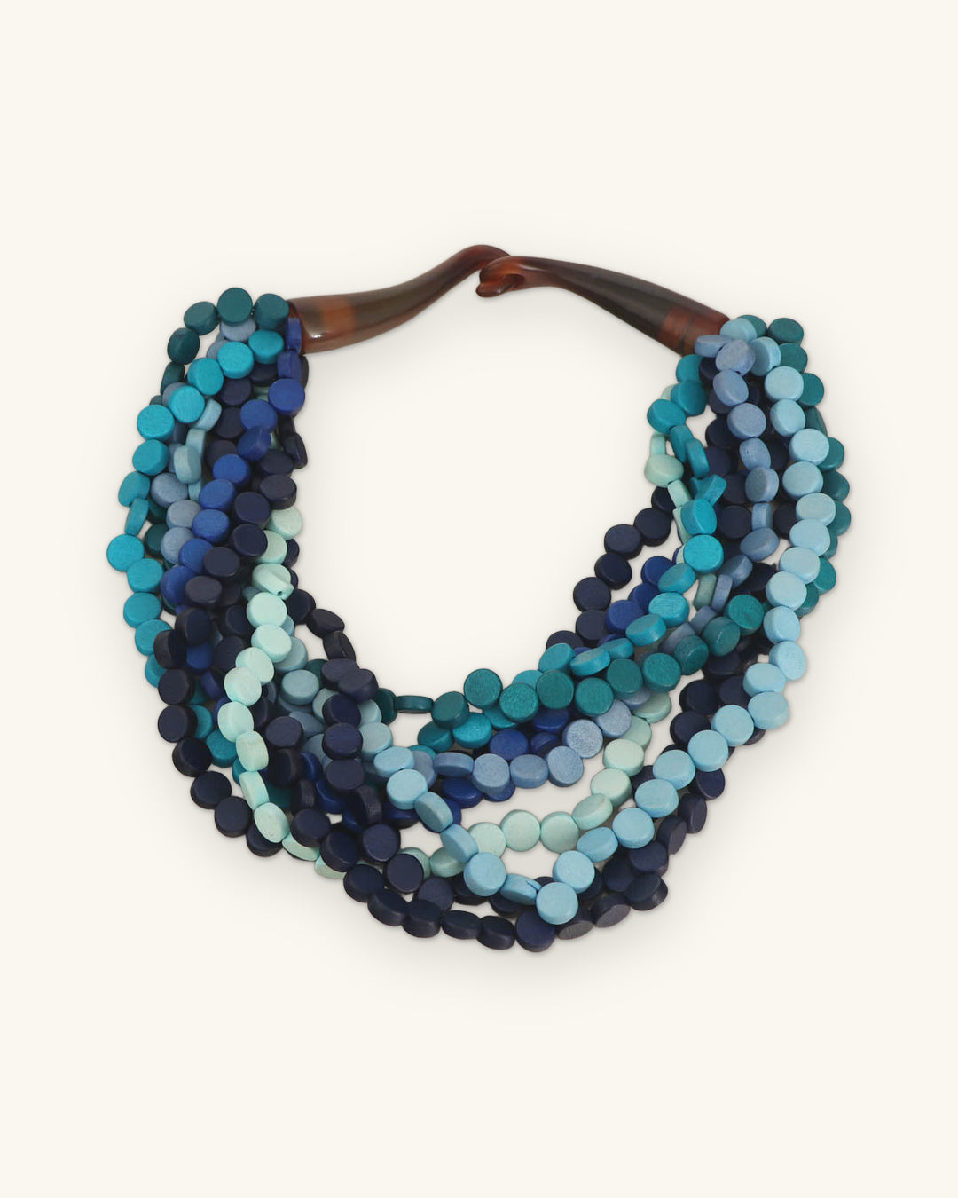 Twisted wood disc necklace in navy, cobalt, teal and pale aqua with a curved horn clasp, laid flat, shown on a sand background
