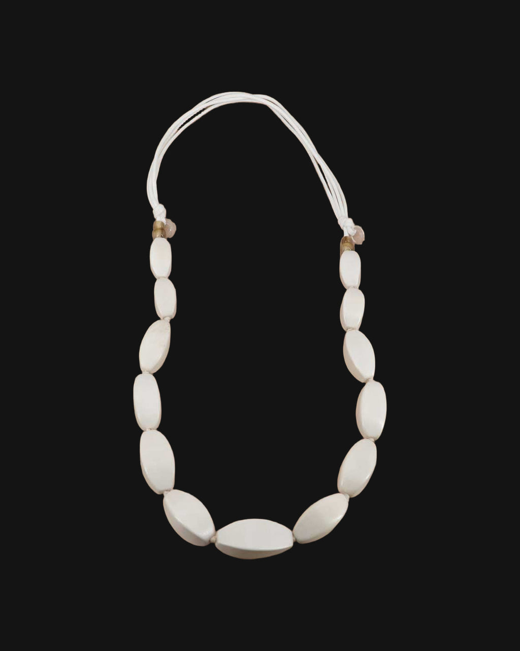 Graduated oval wood bead necklace in soft white on multi-strand cotton cord, handcarved in the Philippines, shown on a black background