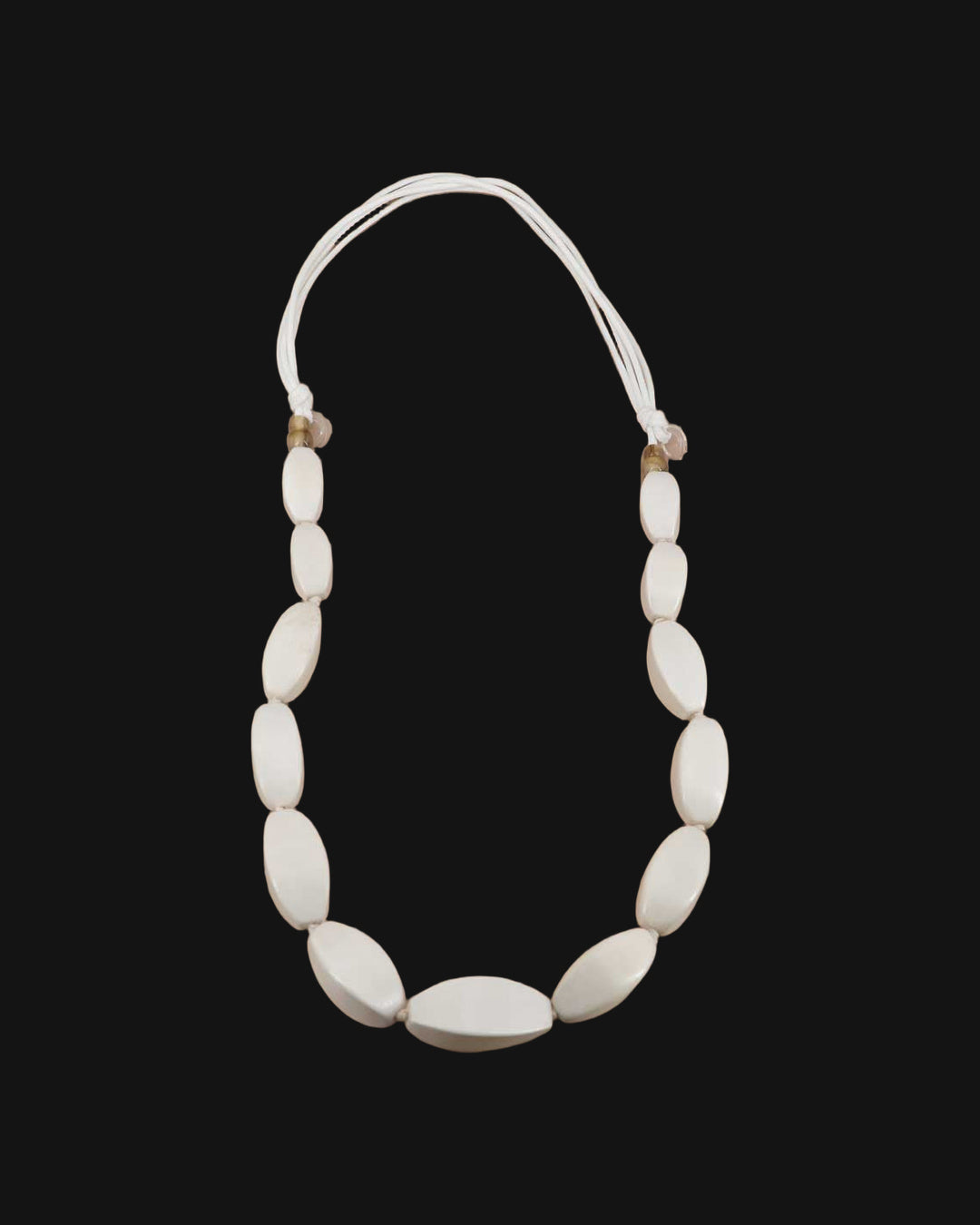 Graduated oval wood bead necklace in soft white on multi-strand cotton cord, handcarved in the Philippines, shown on a black background