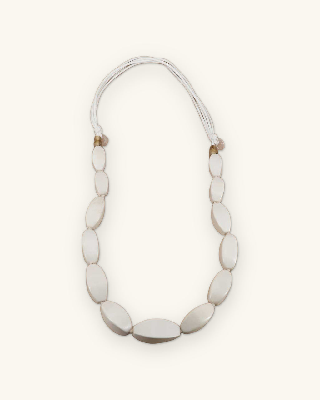 Graduated oval wood bead necklace in soft white on multi-strand cotton cord, handcarved in the Philippines, shown on a sand background