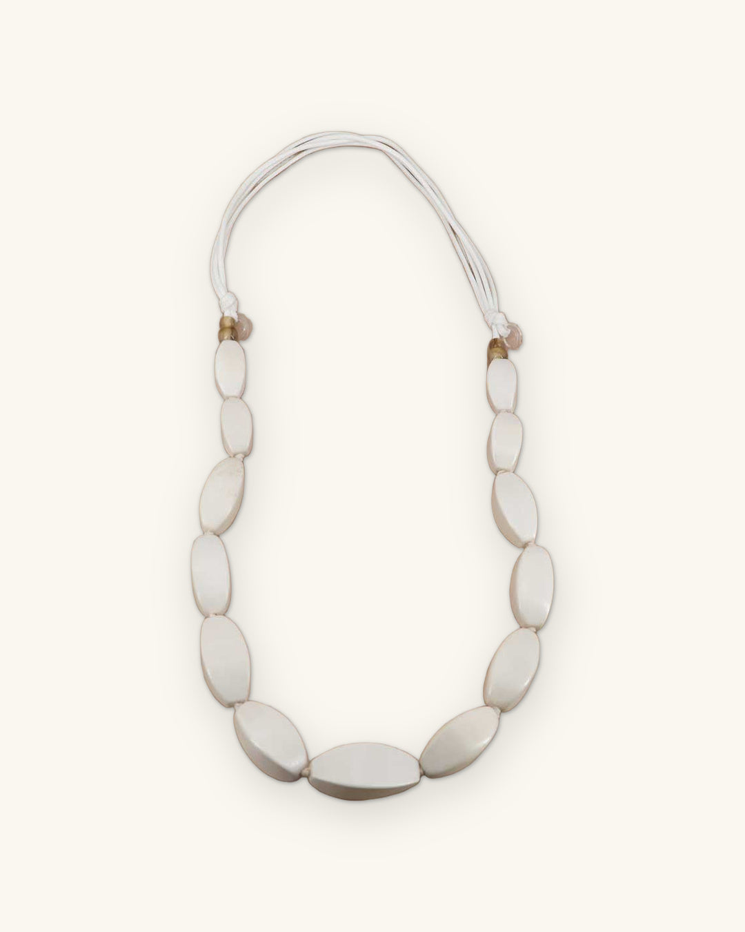Graduated oval wood bead necklace in soft white on multi-strand cotton cord, handcarved in the Philippines, shown on a sand background