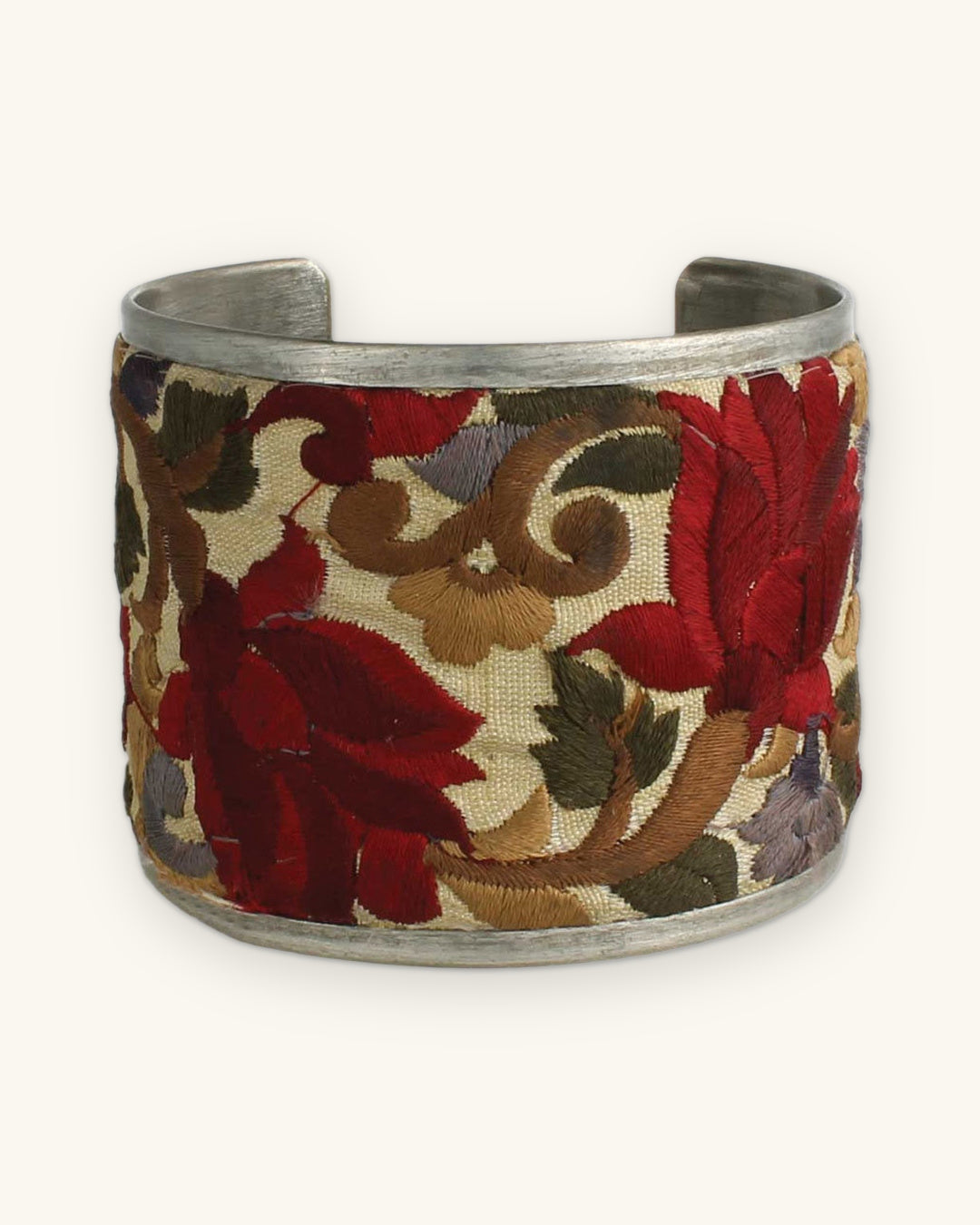 Front of the crimson embroidered cuff with red blooms, olive leaves and lavender flowers, shown on a sand background