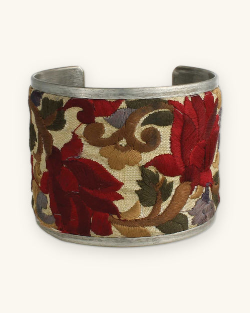 Front of the crimson embroidered cuff with red blooms, olive leaves and lavender flowers, shown on a sand background