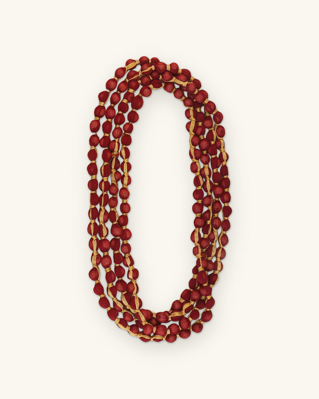 Crimson bead rope necklace coiled into a triple oval, showing beige thread wrapping between beads, shown on a sand background
