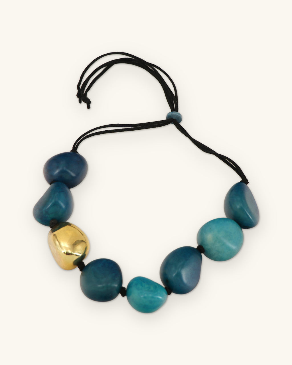 Teal tagua nugget necklace laid flat with black cord ends looped above the sliding bead, shown on a sand background
