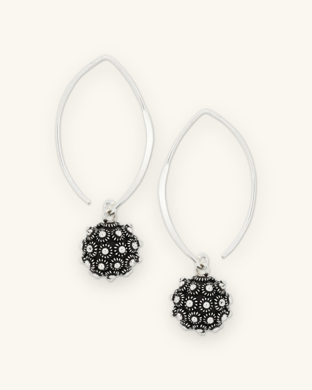 Pair of oxidized silver floret ball earrings on open marquise-shaped sterling silver threaders, shown on a sand background