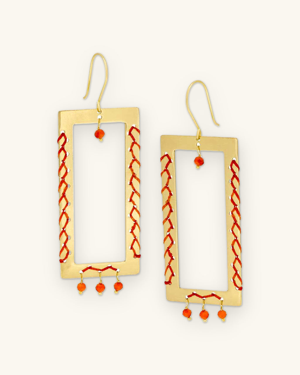 Brass rectangle frame drop earrings laced with orange thread and carnelian bead drops, handmade in India, shown on a sand background