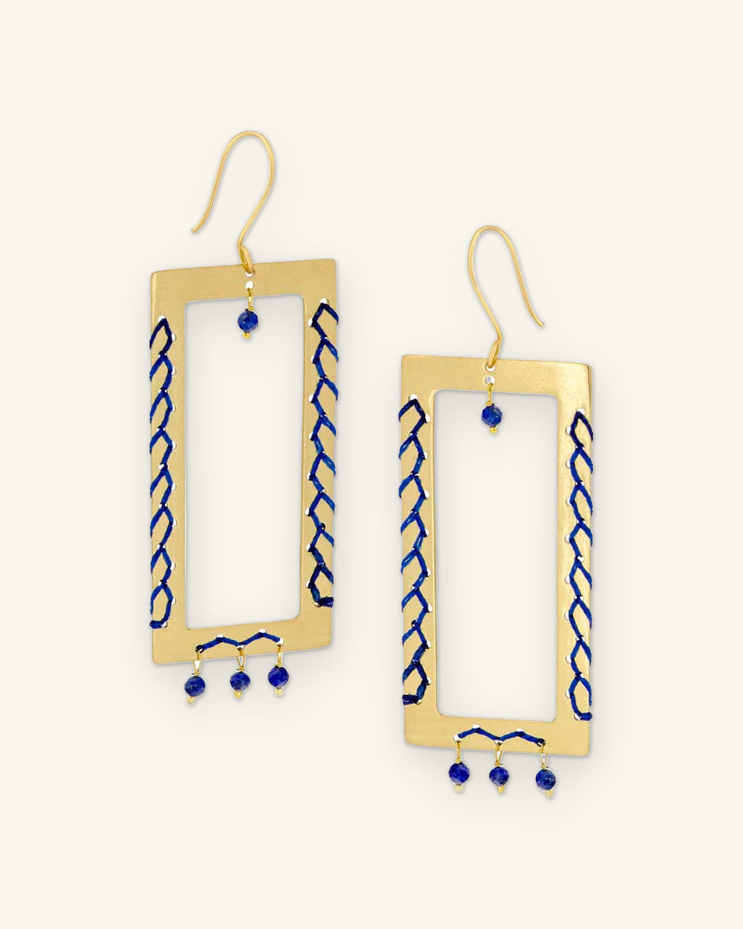 Brass rectangle frame earrings laced with cobalt cord and lapis lazuli bead drops, handmade in India, shown on a sand background